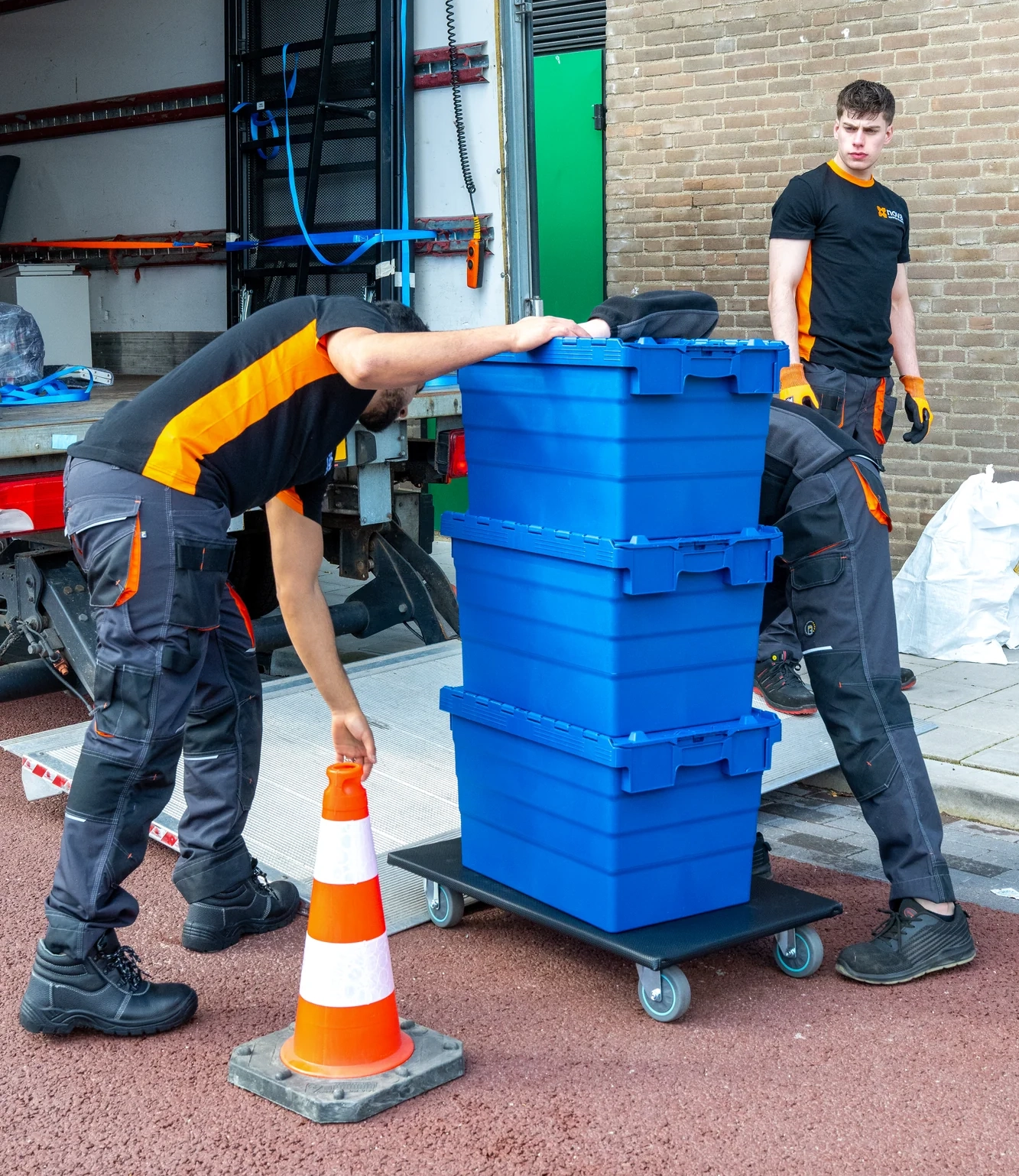 Twee medewerkers stapelen blauwe verhuiskratten op een transportkar tijdens een woningontruiming na overlijden