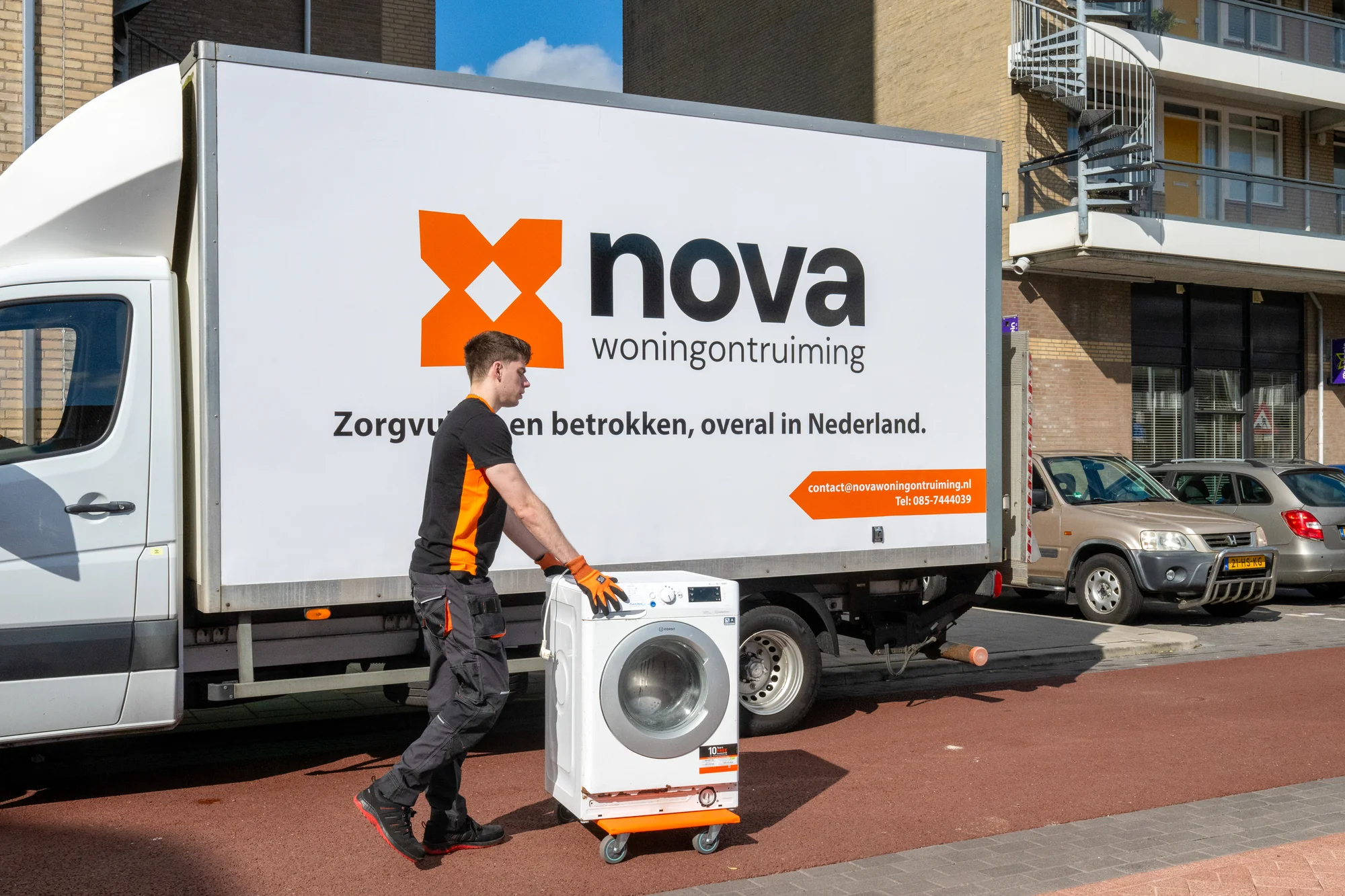Nova-medewerker rolt wasmachine op transportwagen naar vrachtwagen tijdens woningontruiming in Nederland