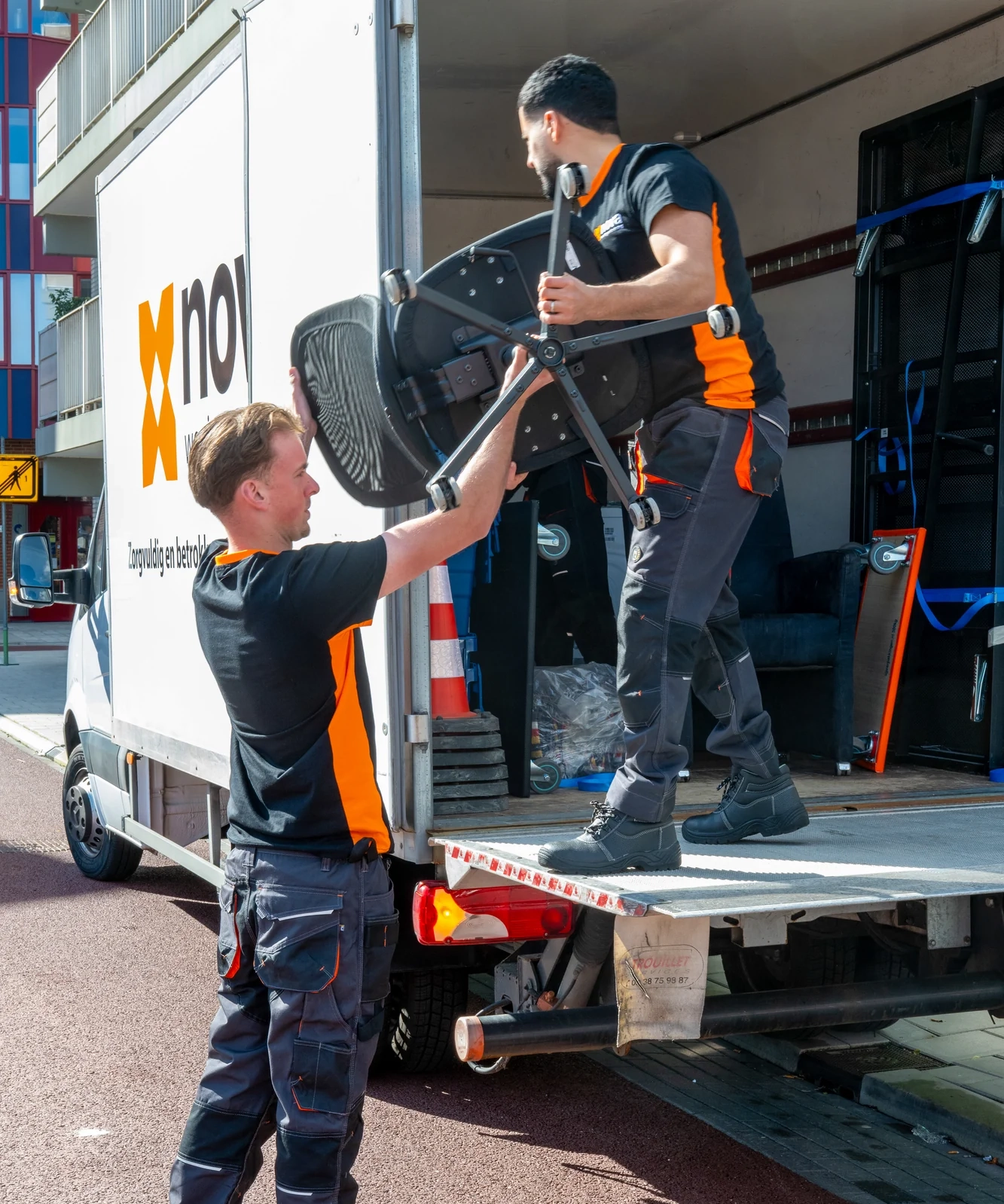 Twee medewerkers laden kantoorstoelen uit een vrachtwagen tijdens een spoedontruiming van een bedrijfspand