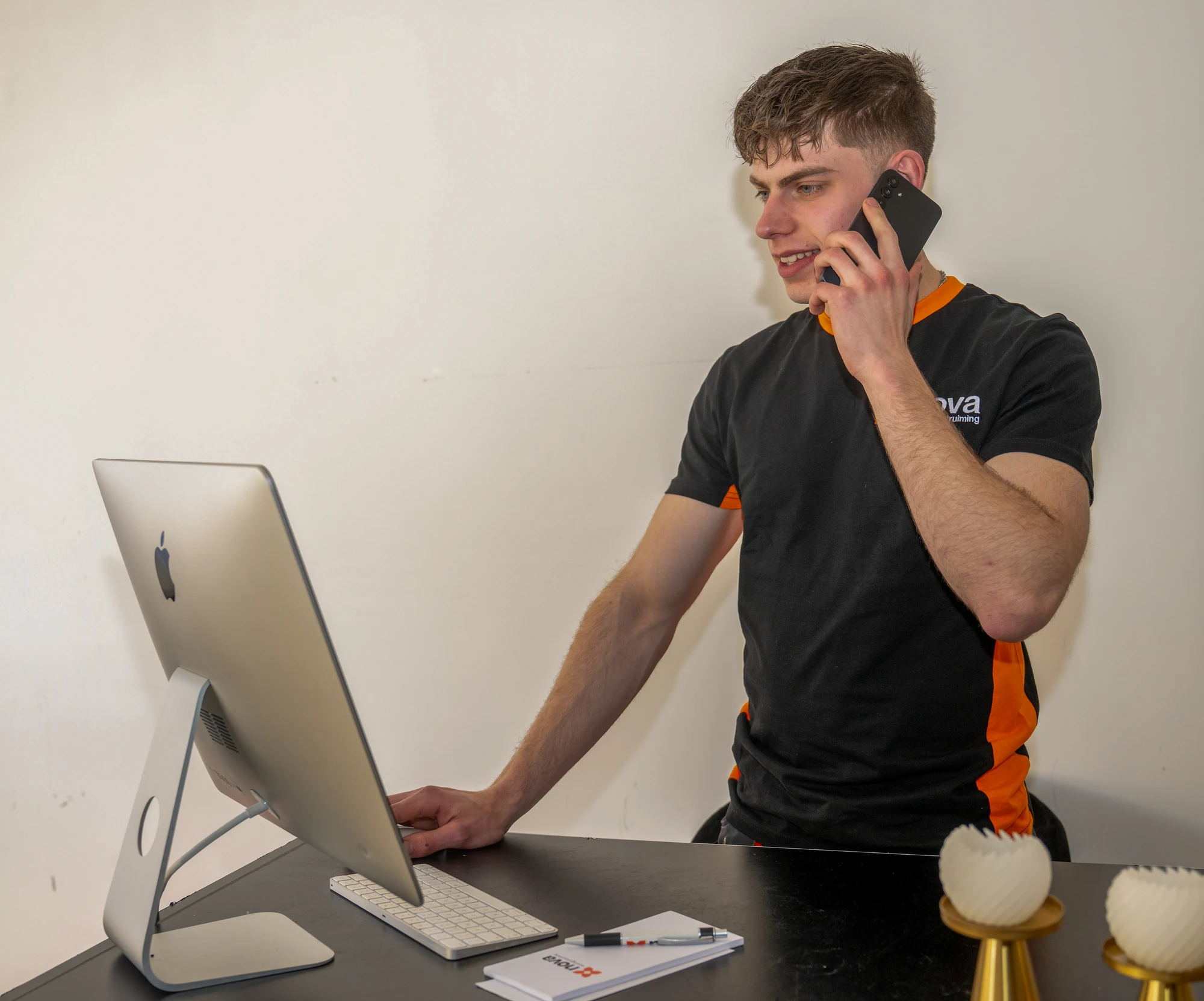 NOVA medewerker in bedrijfsshirt belt staand achter iMac bij woningontruiming Woerden opdracht