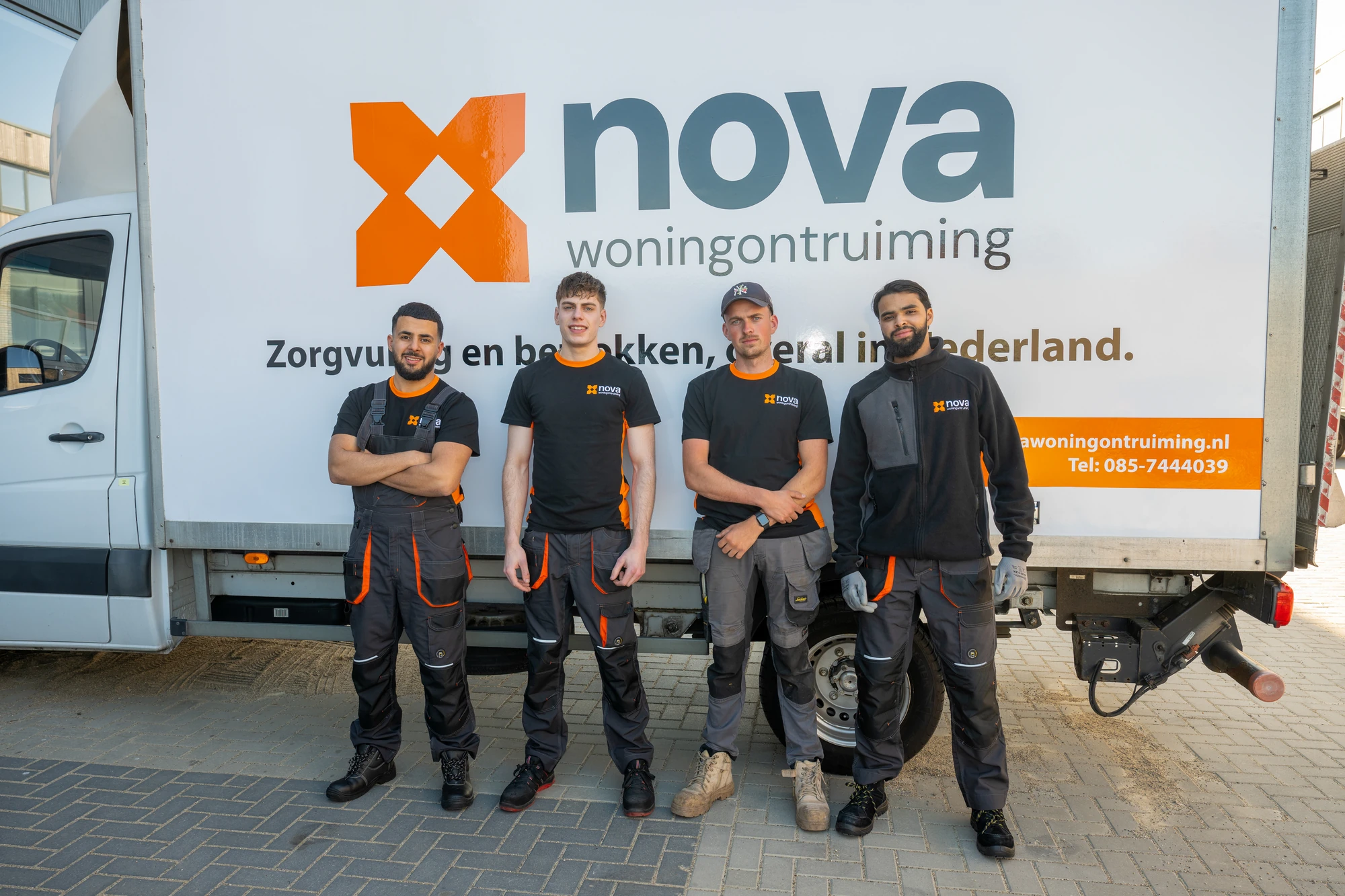 Vier medewerkers van NOVA Woningontruiming in werkkleding poseren voor de witte bedrijfsbus