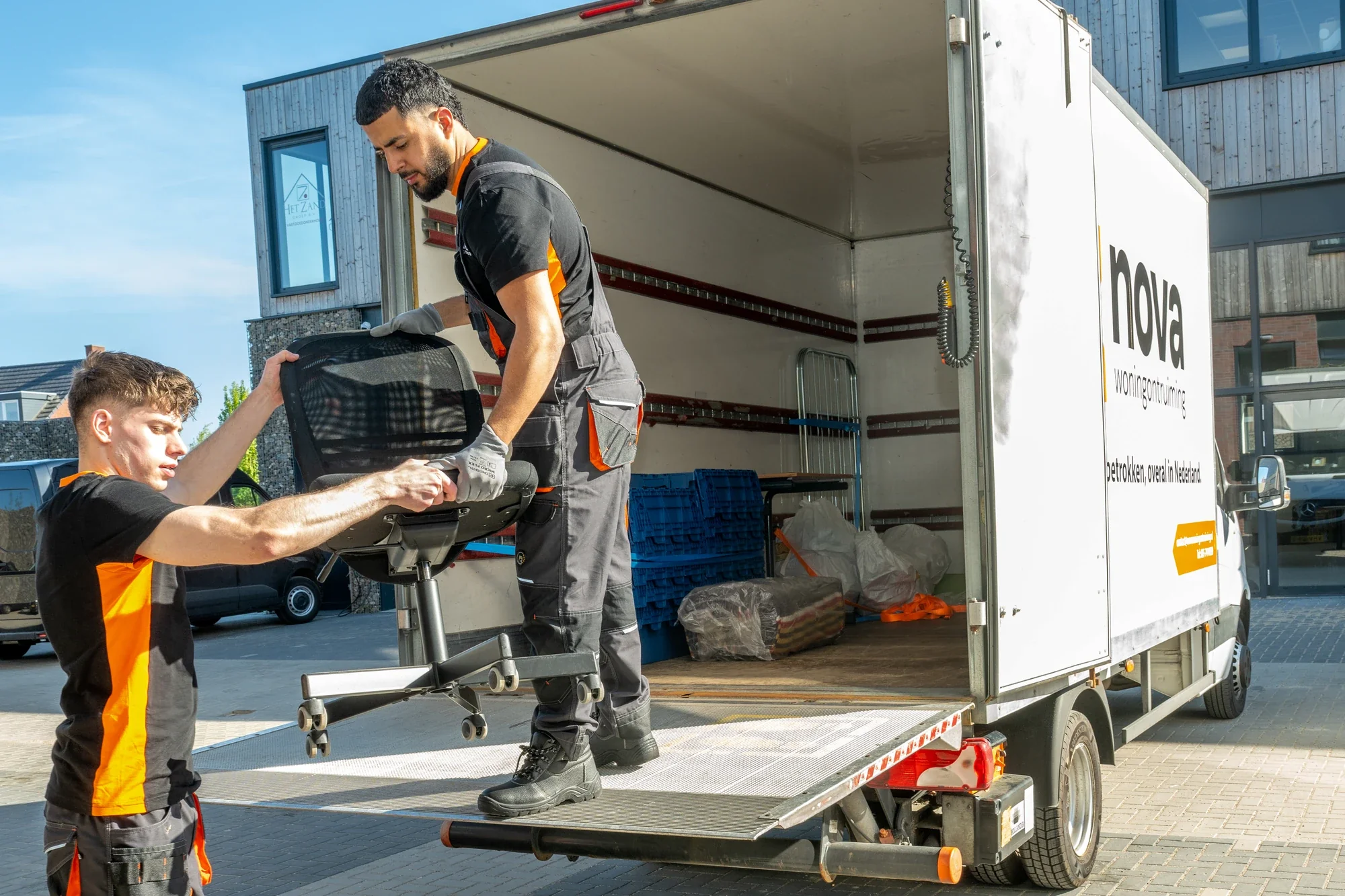 Two Nova staff setting an office chair on the tail lift of a box truck