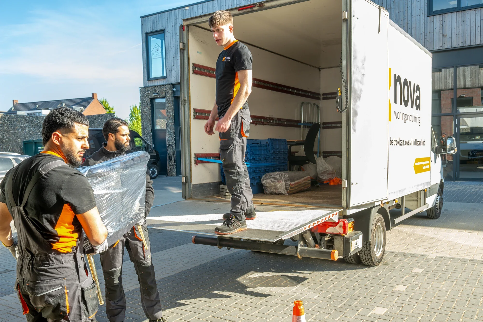 Two Nova staff carrying a wrapped item of furniture to the tail lift of the box lorry