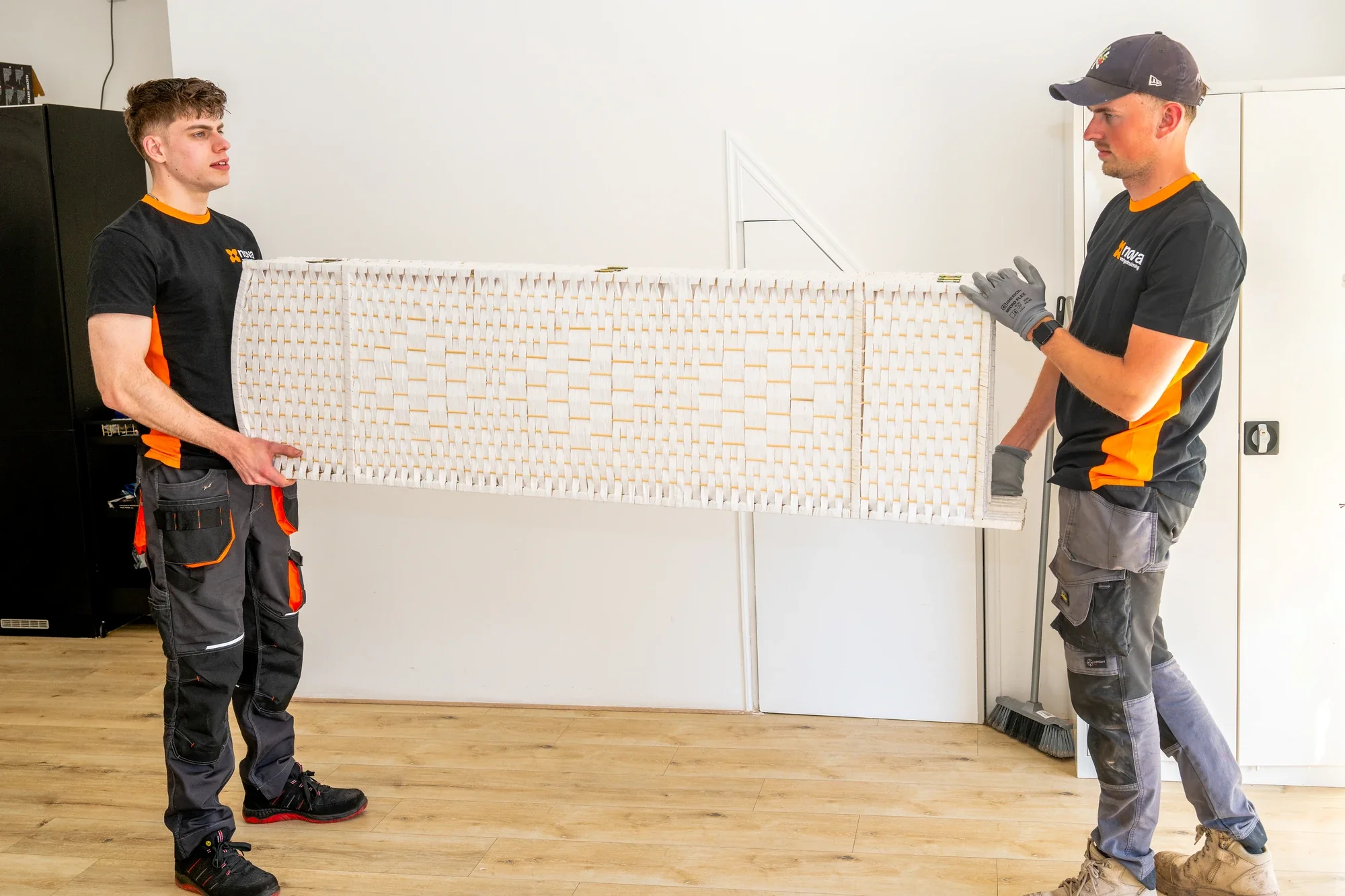 Two Nova employees carrying a large white room divider through an empty room