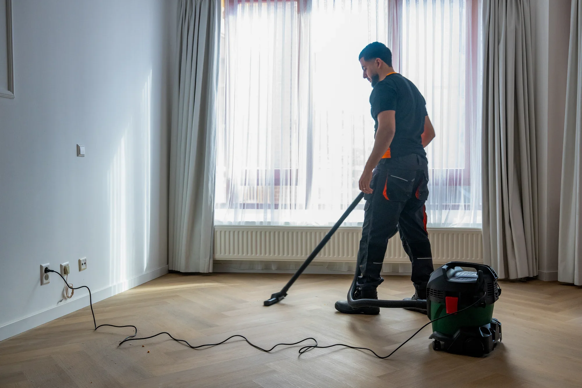 A Nova staff member vacuuming the floor of an empty room with the industrial vacuum cleaner
