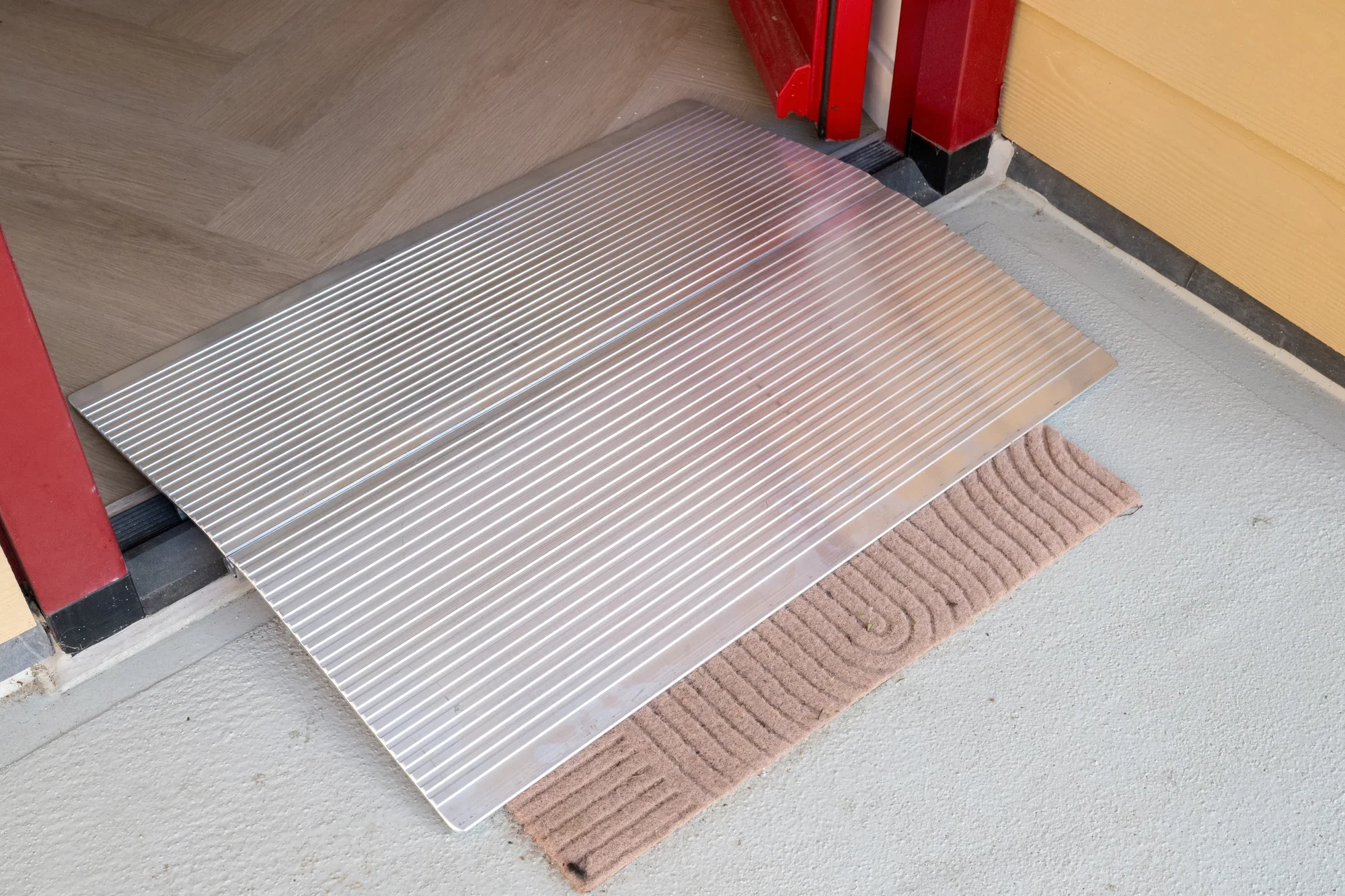 An aluminium loading ramp over a threshold at a front door with a red frame post