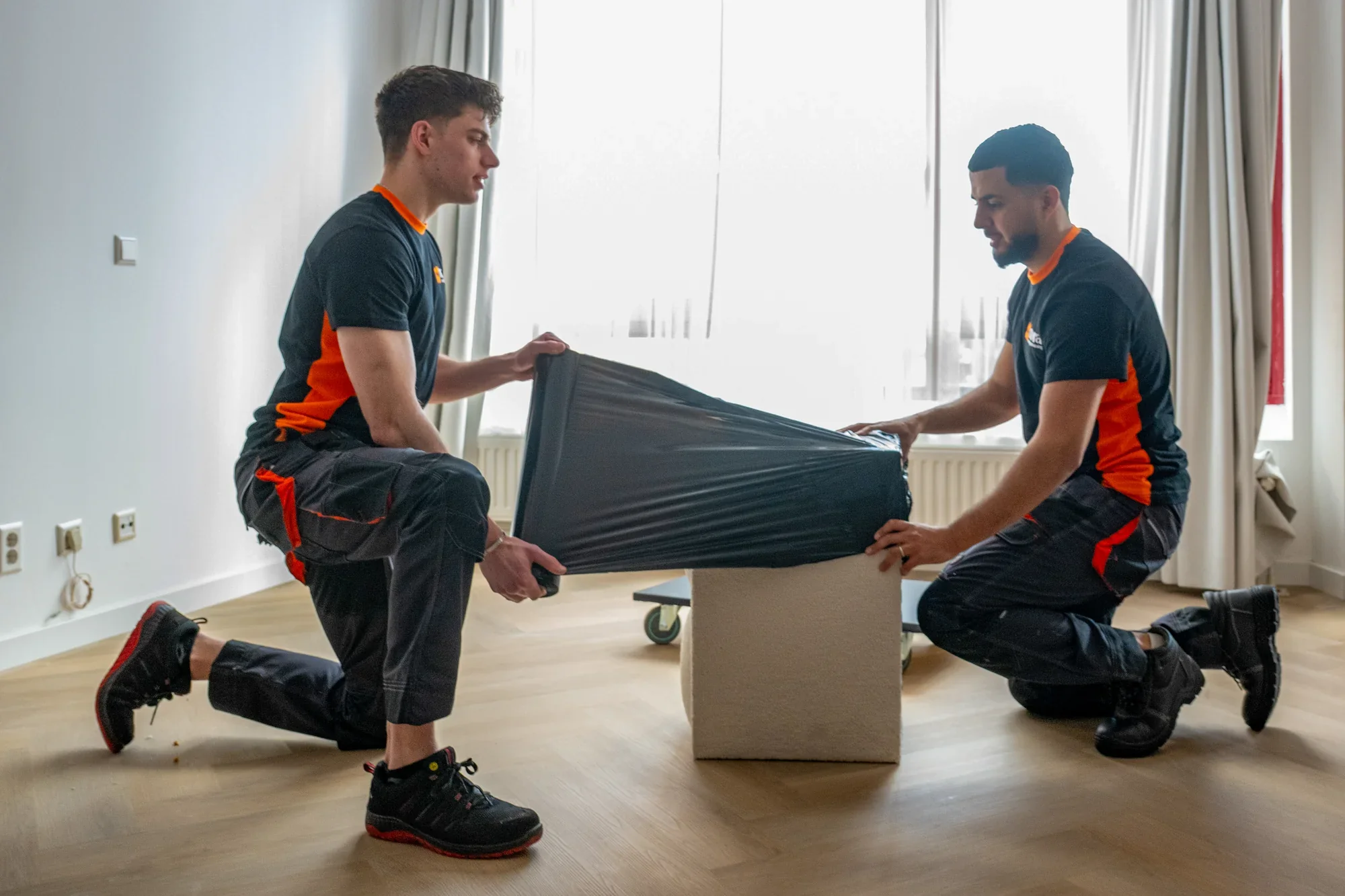 Two Nova staff wrapping a footstool in black film