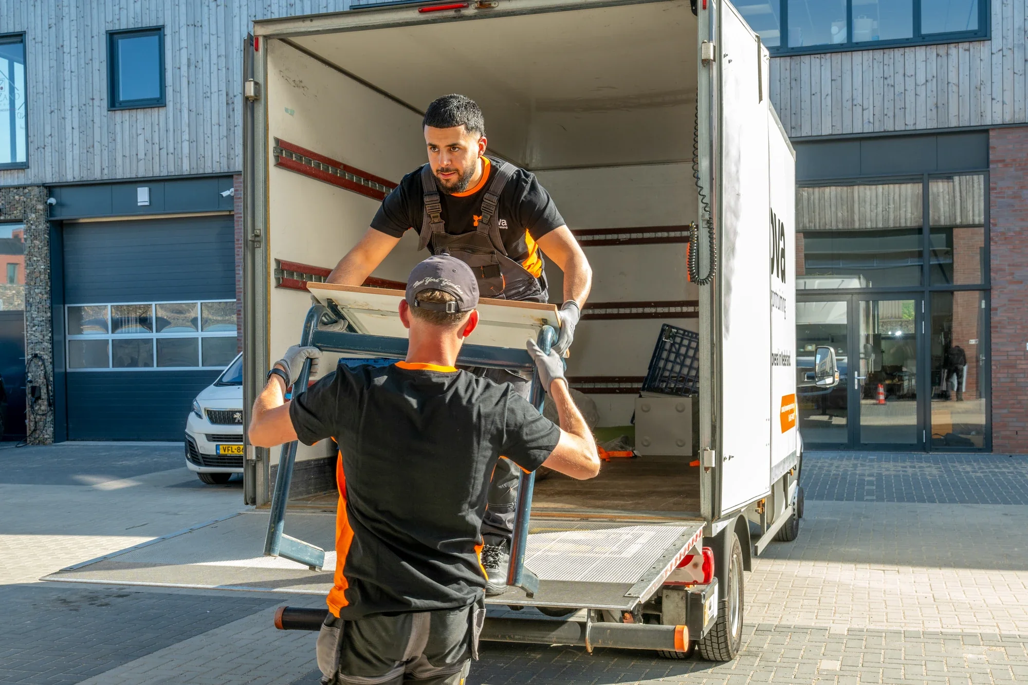 Two Nova staff members sliding a table into the box lorry over the tail lift