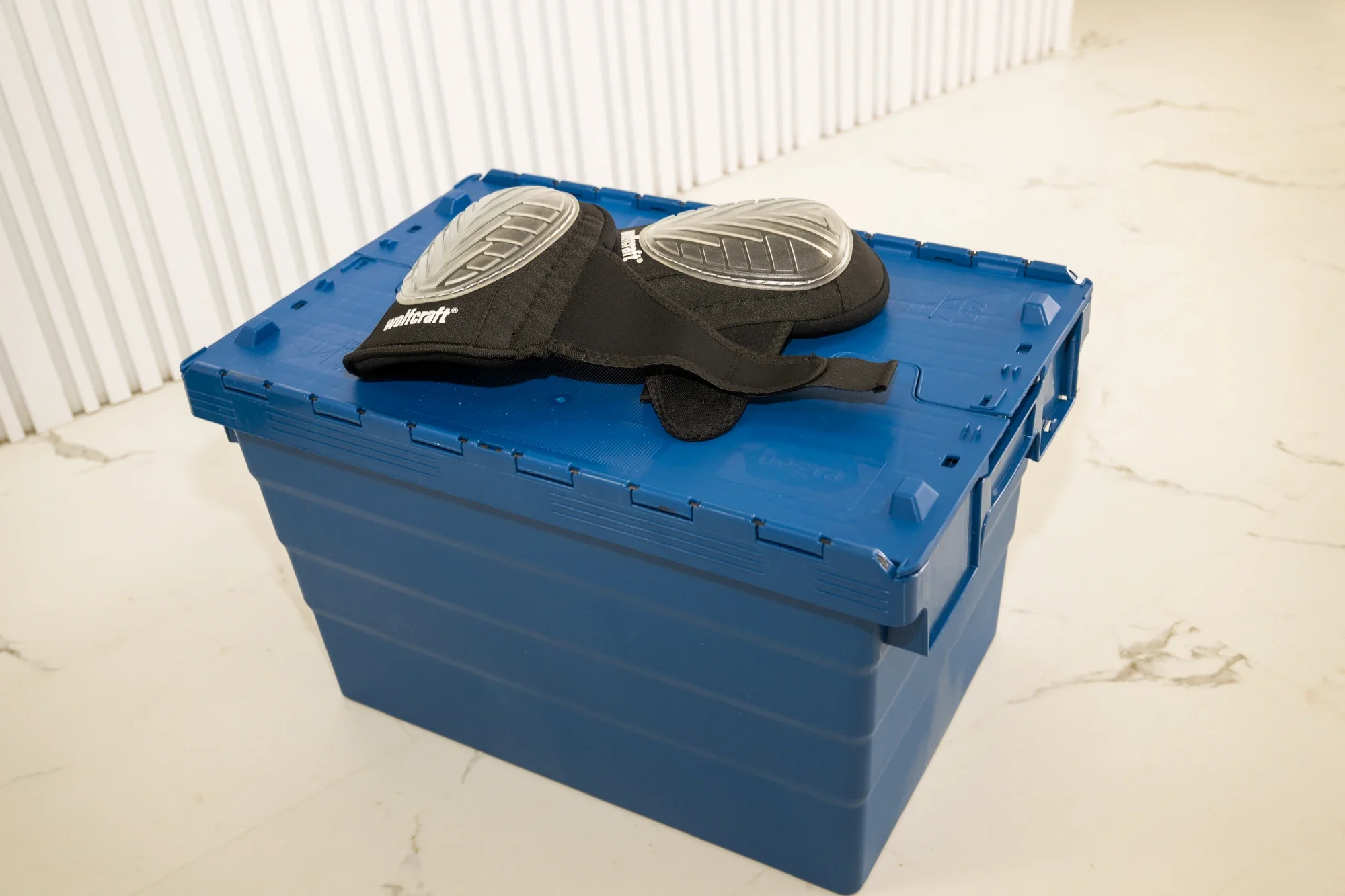 A blue moving crate with a pair of knee pads on top