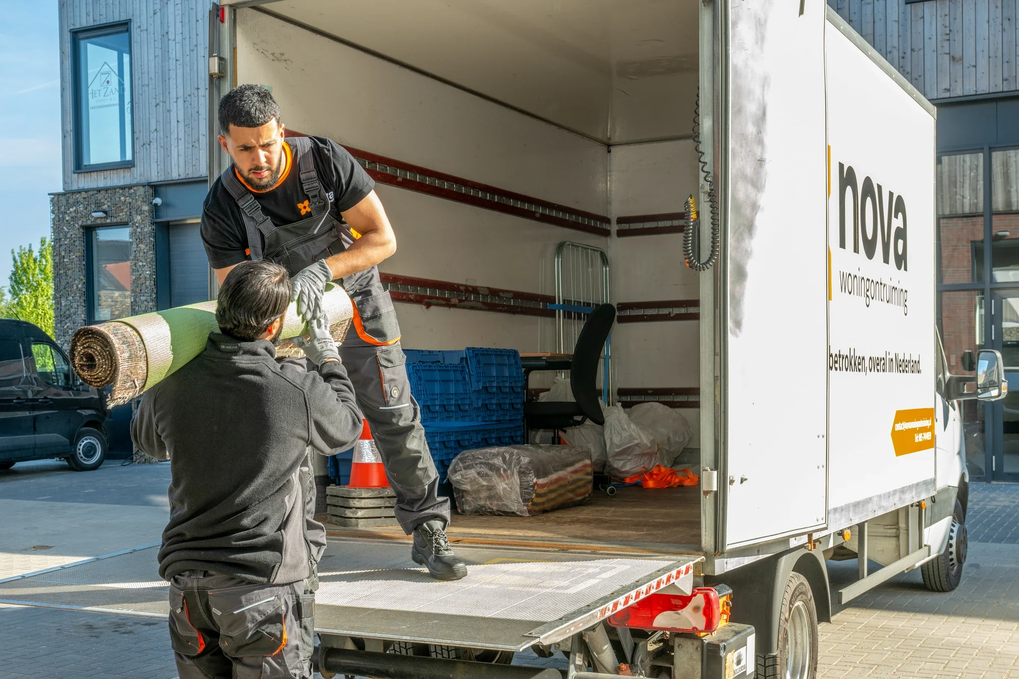 Two Nova staff lifting a rolled up rug onto the tail lift