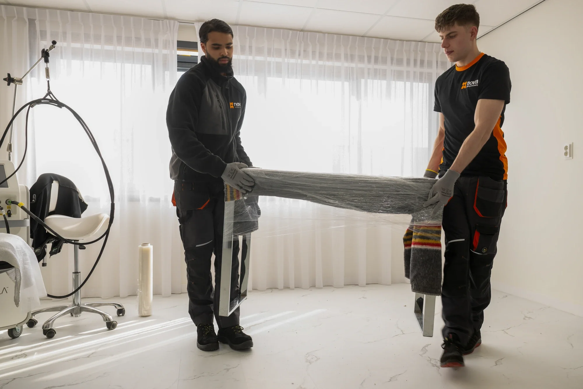 Two Nova staff members carrying a table wrapped in film through an empty room